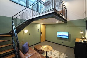 Un salon moderne avec un escalier, un téléviseur à écran plat, une table basse et un canapé en cuir.