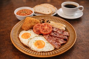 Een bord met eieren, spek, tomaten en toast, vergezeld van een kop koffie en een kom bonen.