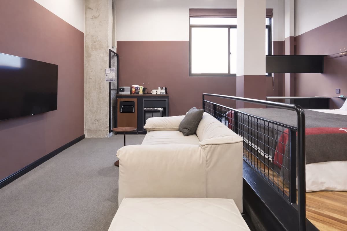 Een moderne hotelkamer met een groot flatscreen televisietoestel, een bank, een klein tafeltje en een raam.