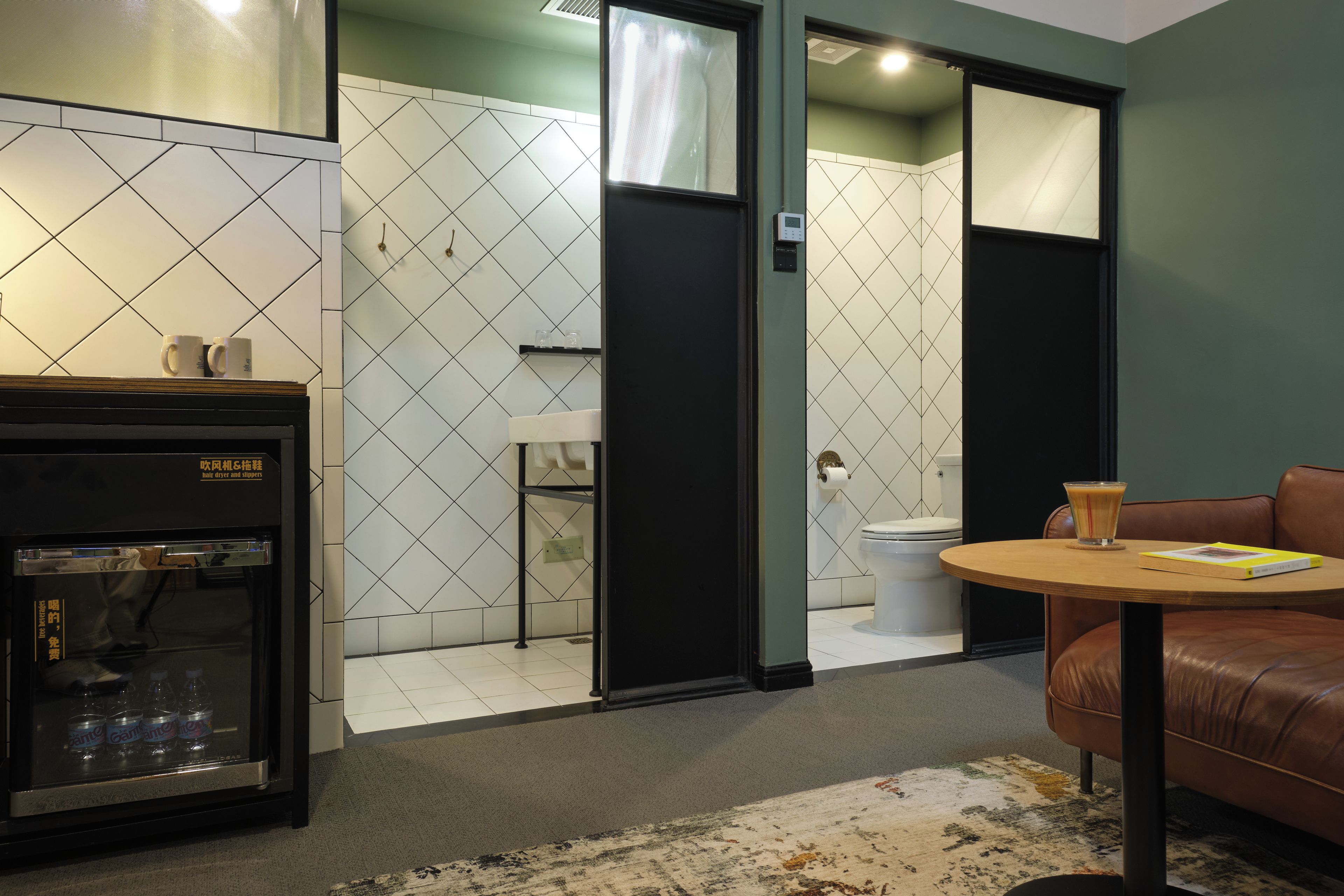 Ein modernes Badezimmer mit Toilette, Waschbecken und Duschbereich. Auf einem Tisch stehen eine Kaffeemaschine und ein Glas Wasser.