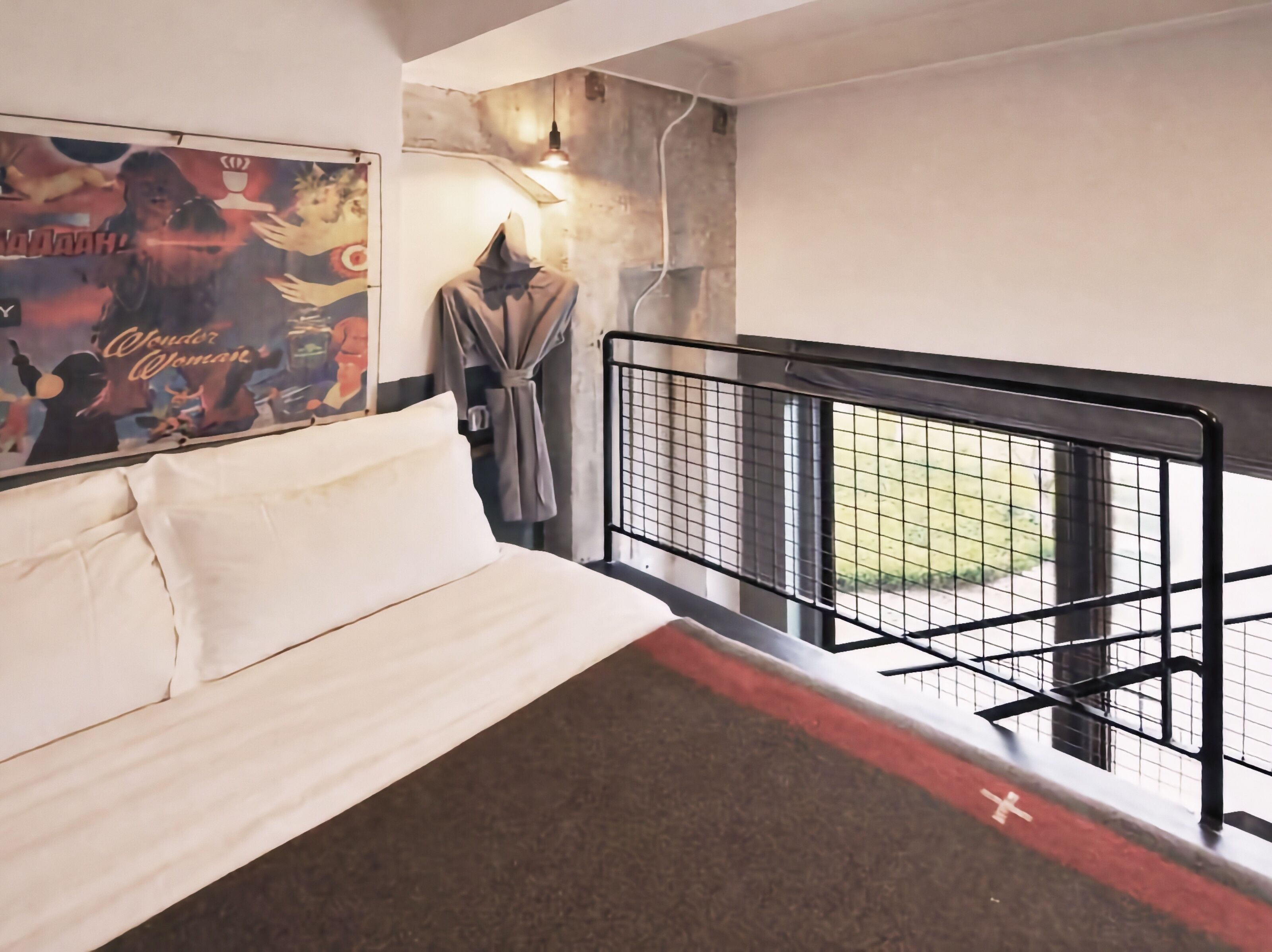 A hotel room with a bed, a poster on the wall, a robe hanging, and a balcony with a railing.