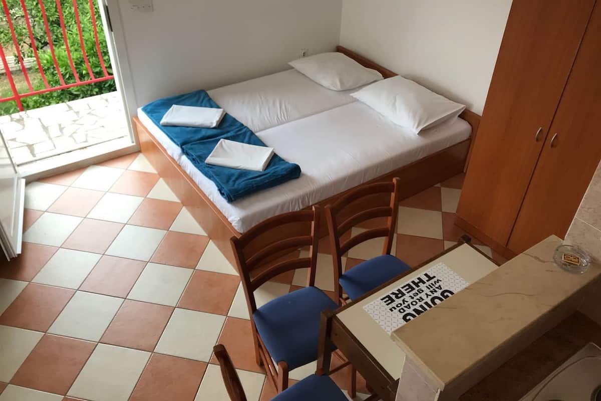 Ein kleiner, ordentlich eingerichteter Raum mit einem Bett, zwei Stühlen, einem Tisch und einem Schrank.