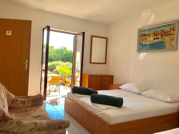 A bedroom with a bed, a chair, a desk, and a view of the outdoors.