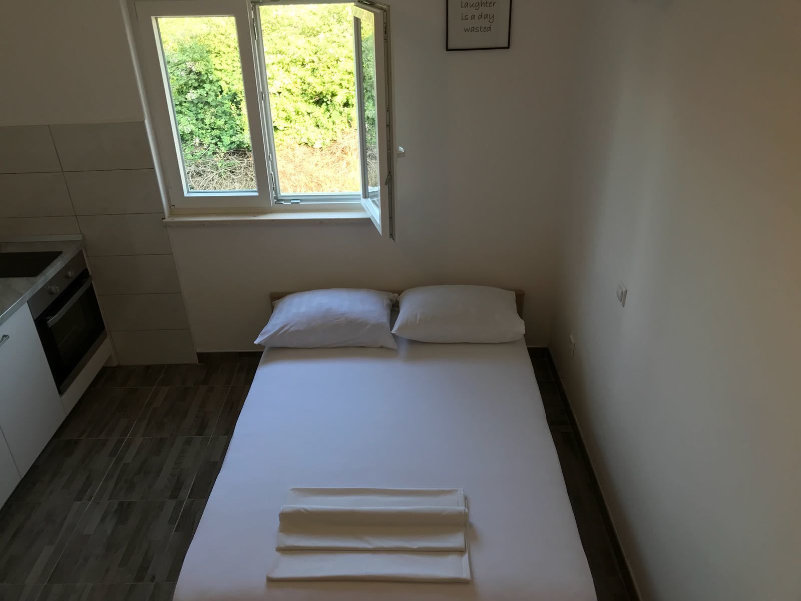A small, clean room with a bed, a window, and a kitchenette.
