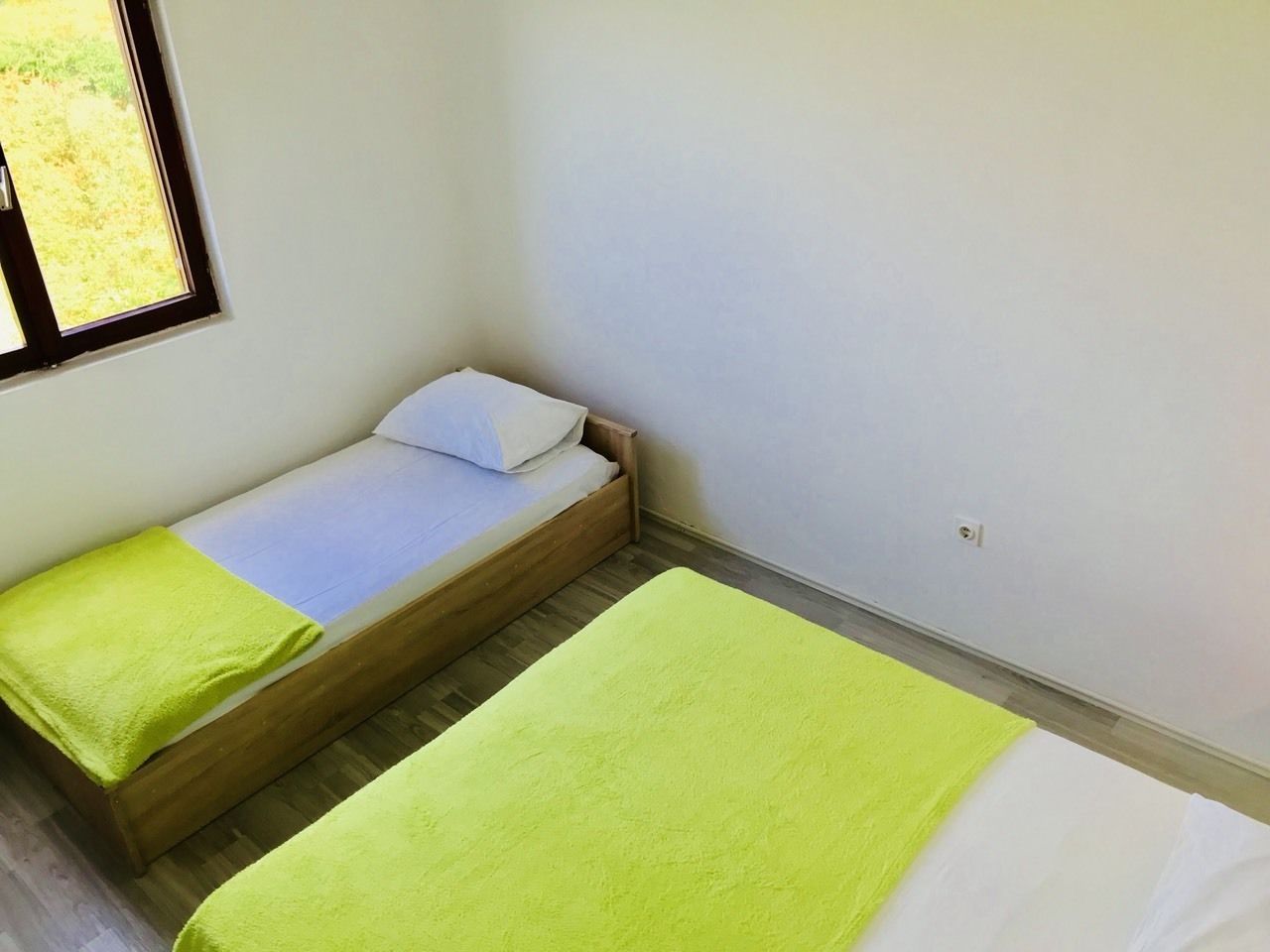 A small, single-bed room with a wooden frame, a white mattress, and a green blanket.