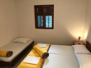 A room with two single beds, a window with wooden frames, and a bedside lamp.