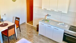 A modern kitchen with white cabinets, a sink, and a countertop. There is a dining table with chairs and a clock on the wall. - Sreser Dubrovnik Apartments Urlic (Janjina)