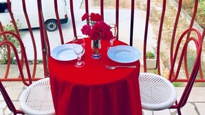 A balcony with a red table set for two, overlooking a coastal road and a white building. - Sreser Dubrovnik Apartments Urlic (Janjina)