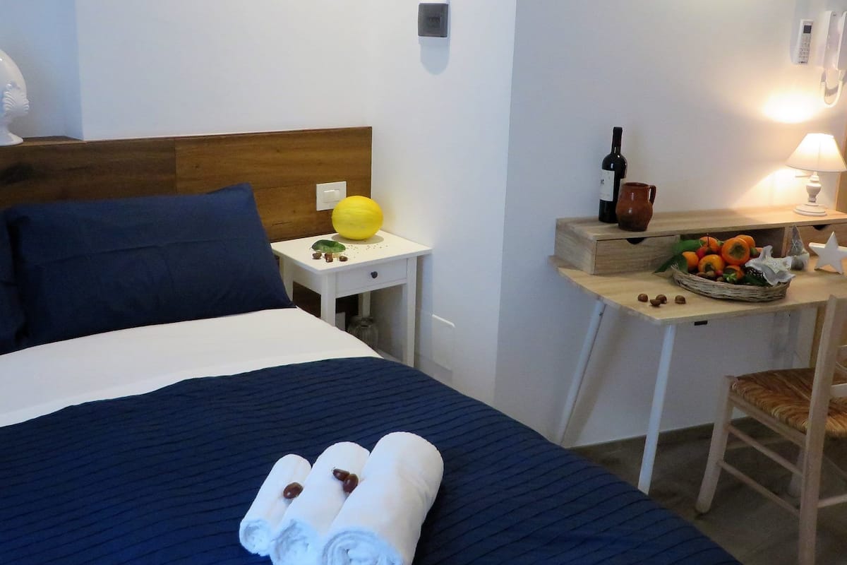 Ein Hotelzimmer mit einem Bett, einem kleinen Tisch mit Lampe, einer Obstschale und einer Weinflasche.