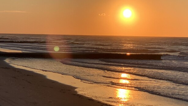 A beach with the sun setting over the ocean, creating a reflection on the wet sand.