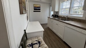 A compact kitchen with white cabinetry, a built-in dishwasher, and a window with blinds.