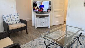 A living room with a television, wicker furniture, and a glass coffee table.