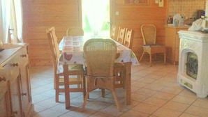 Una zona de menjador acollidora amb taula i cadires de fusta, una cuina amb fogó i una finestra amb cortines.