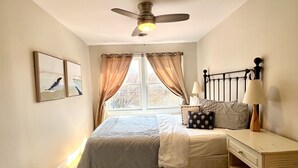 Ein Schlafzimmer mit einem Bett, einem Nachttisch, einer Lampe, einem Deckenventilator und einem Fenster mit Vorhängen.