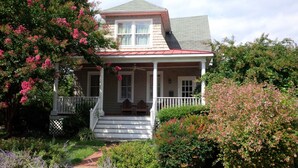 Ein zweistöckiges Haus mit Veranda, überdachter Eingangstür und einem kleinen Garten.