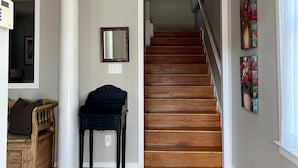 Ein geräumiger Flur mit einer Holztreppe, einer weißen Säule, einem Klavier und einem gerahmten Spiegel.
