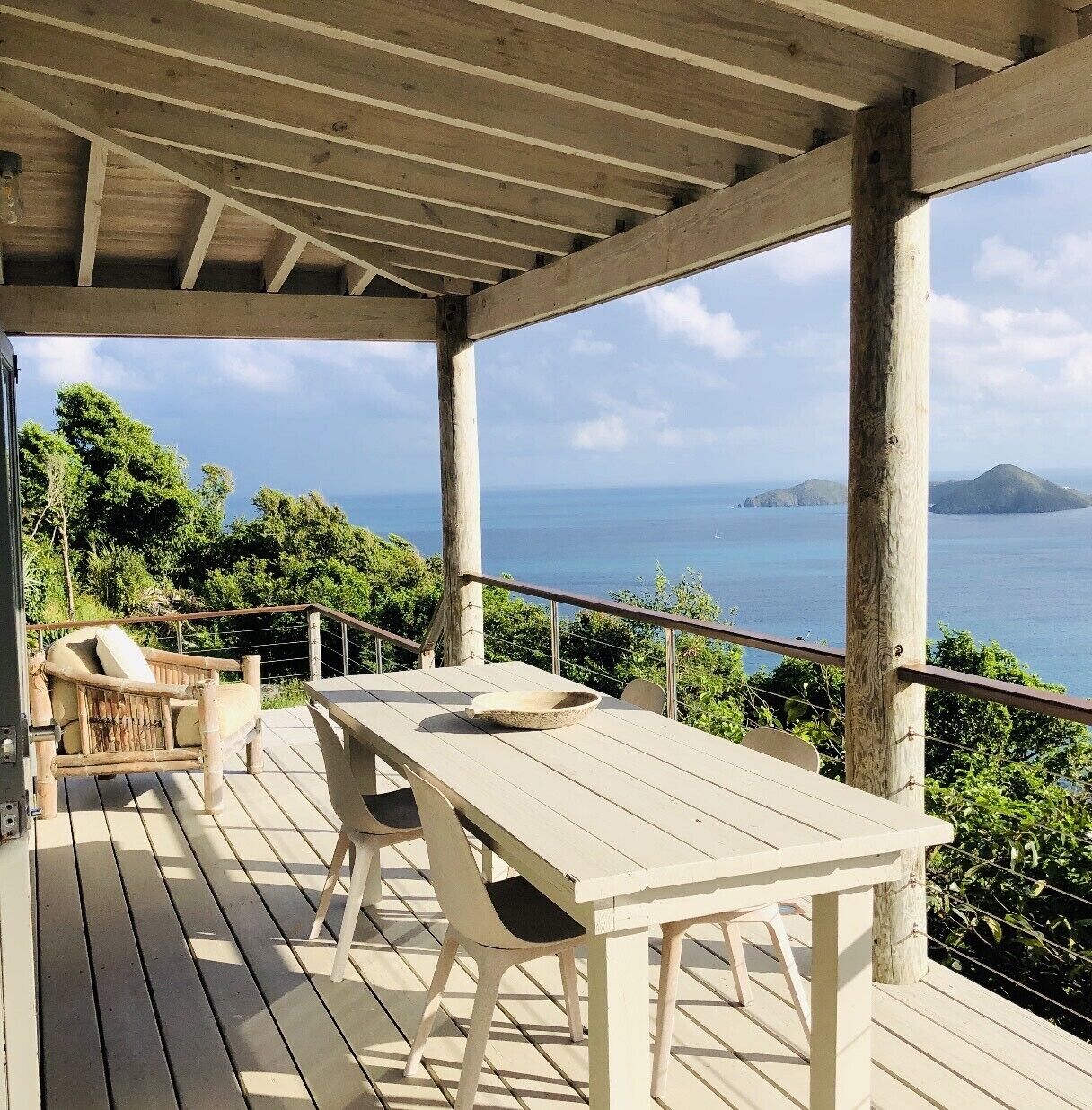 A wooden deck with a table and chairs, overlooking a body of water and greenery.