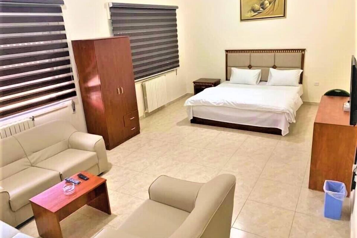A hotel room with a bed, a sofa, a desk, a wardrobe, and a radiator.