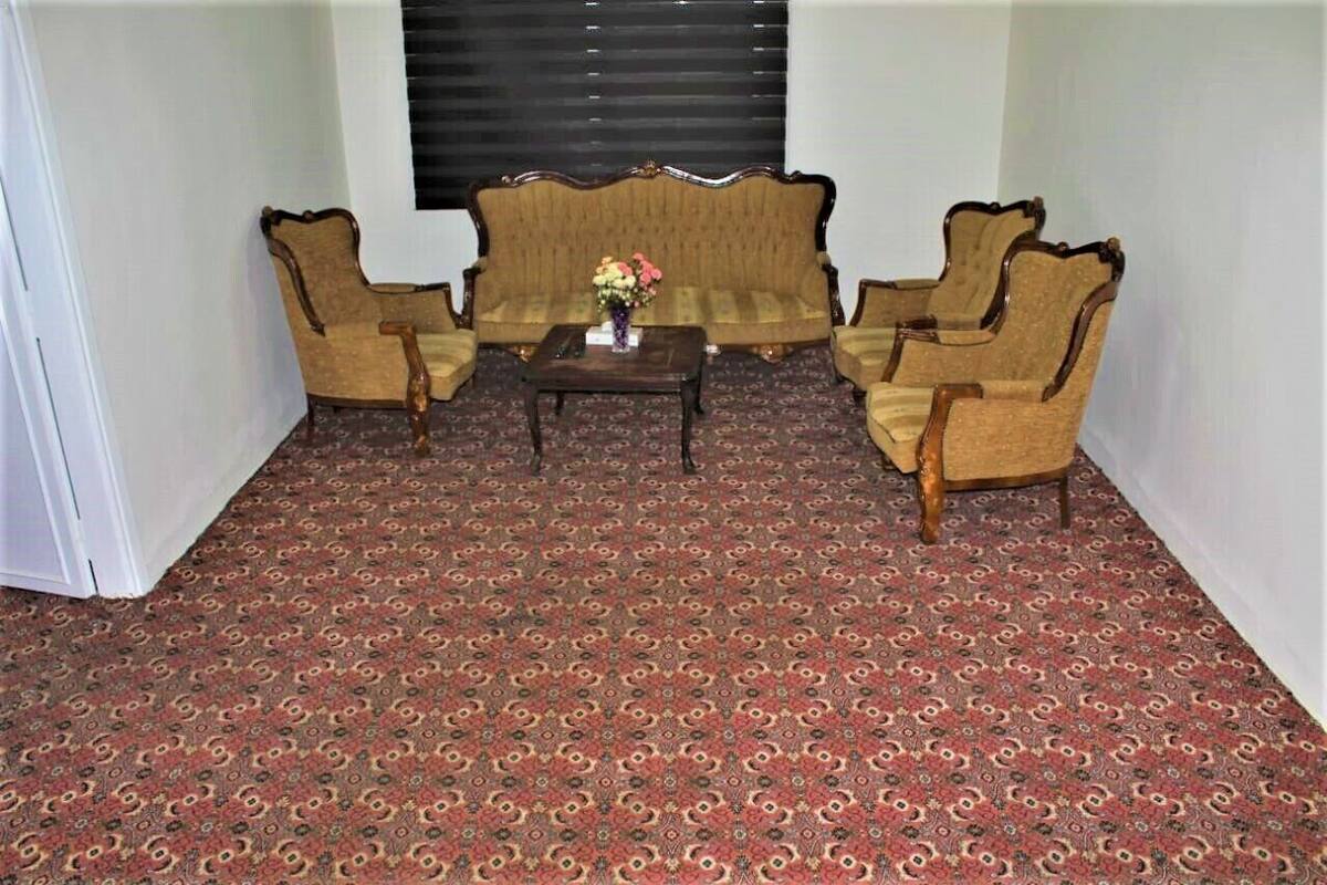 A room with a patterned carpet, a sofa, two armchairs, and a small table with a vase of flowers.