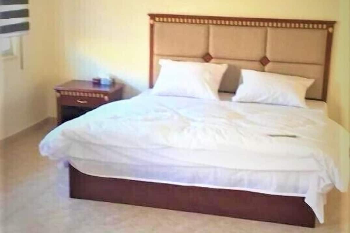 A neatly made bed with a wooden headboard, a small bedside table, and a painting on the wall.