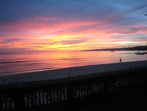 Un coucher de soleil sur une plage, avec une mer calme et une personne qui se promène le long du rivage.