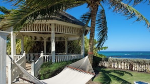 Um gazebo com uma rede, uma palmeira e vista para o oceano.