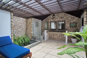 A stone-walled bathroom with a shower, a sink, and a blue cushioned bench. - Villa Paradiso, Mammee Bay, Ocho Rios, Jamaica (Steer Town)