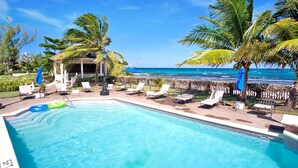 Uma área de piscina com espreguiçadeiras, um bangalô e vista para o oceano.