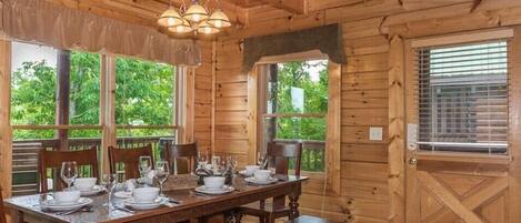 A wooden dining room with a table set for four, large windows, and a wooden ceiling.