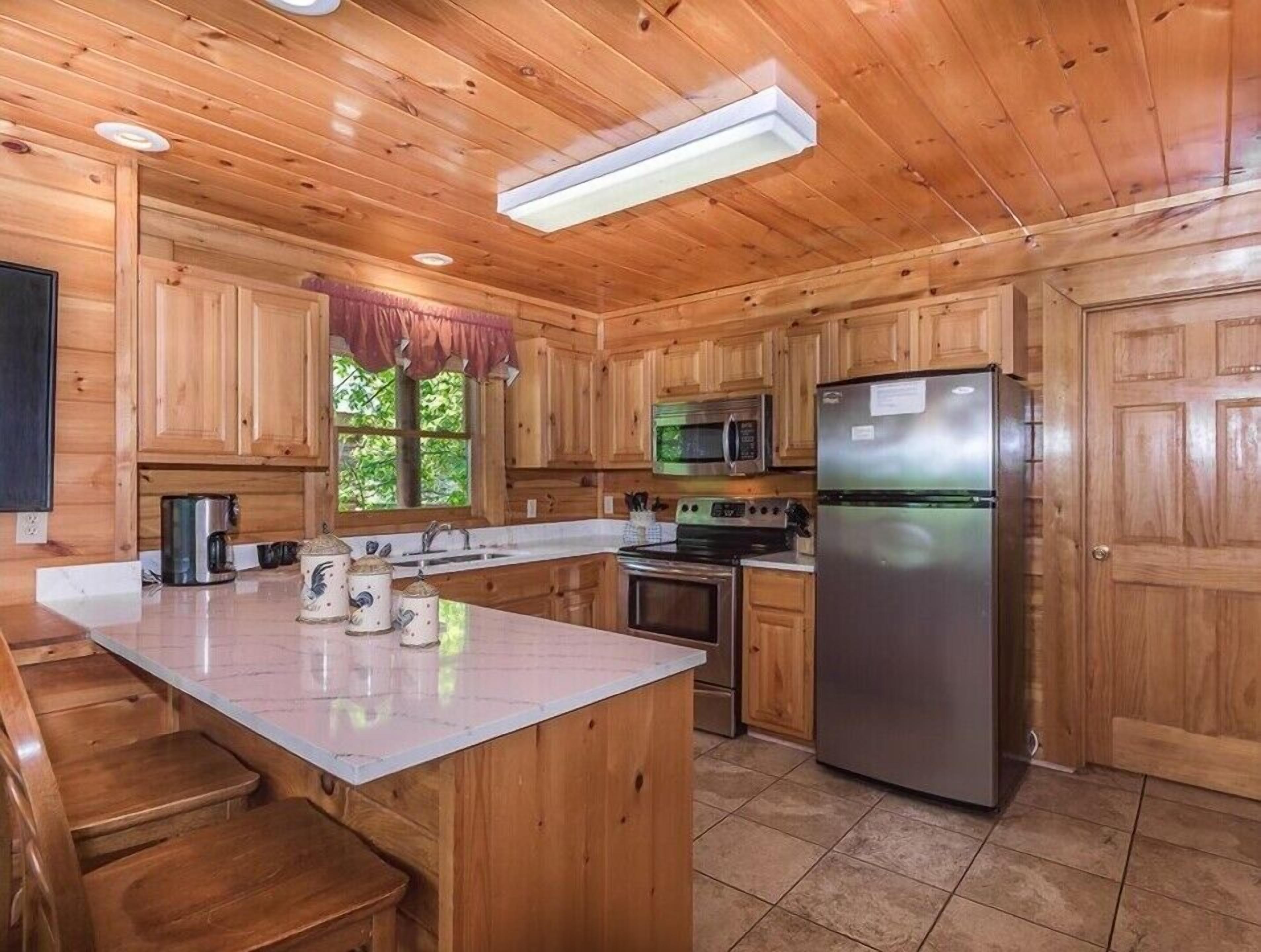 A wooden cabin kitchen with a central island, a refrigerator, a microwave, and a stove.