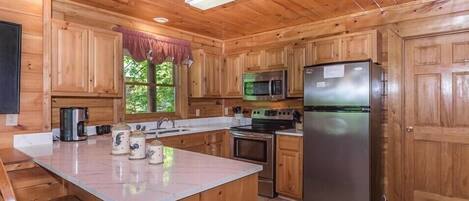 A wooden cabin kitchen with a central island, a refrigerator, a microwave, and a stove.