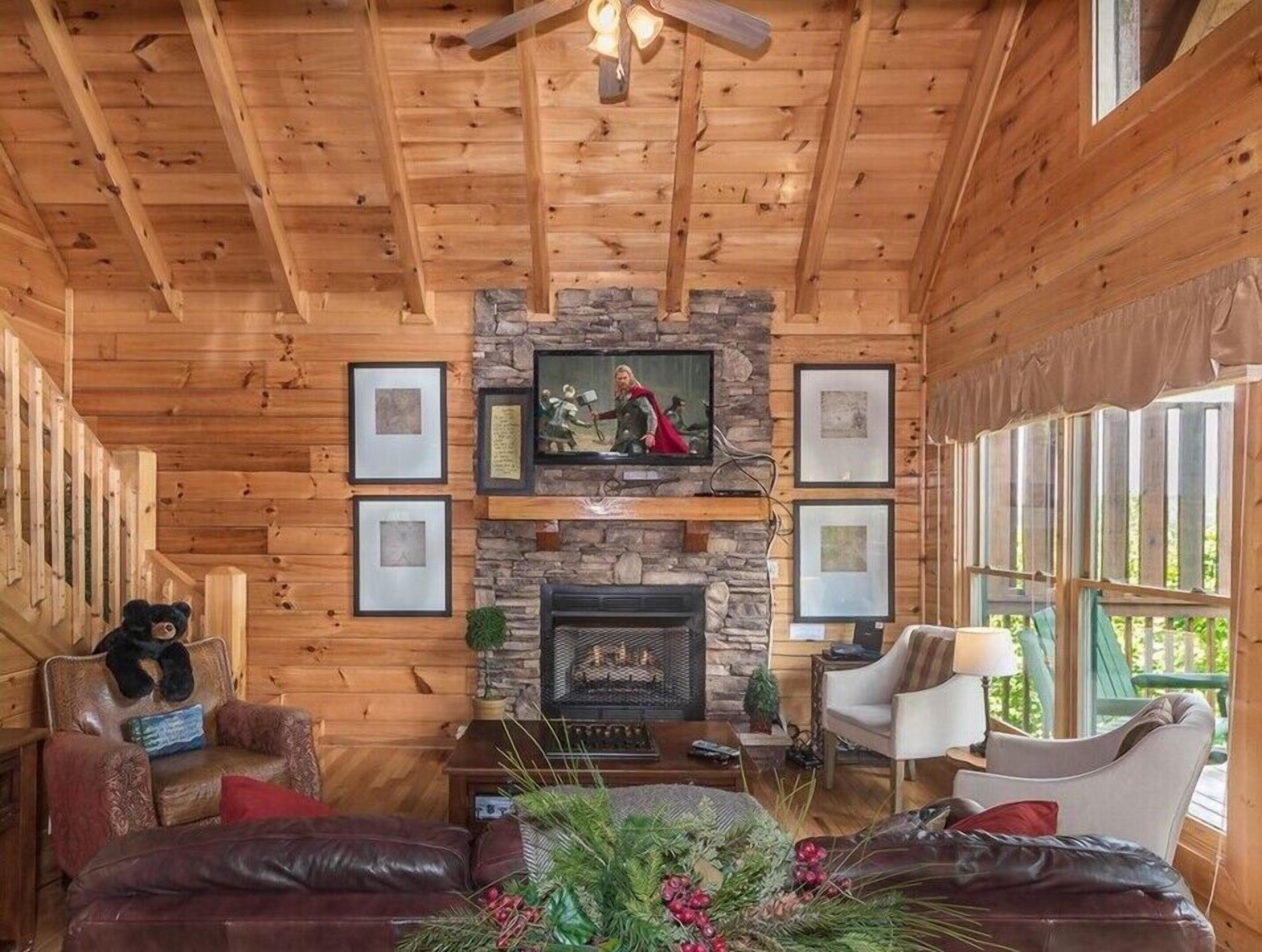 L’intérieur d’une cabane en rondins, avec une cheminée en pierre, des œuvres d’art encadrées et un coin salon confortable.