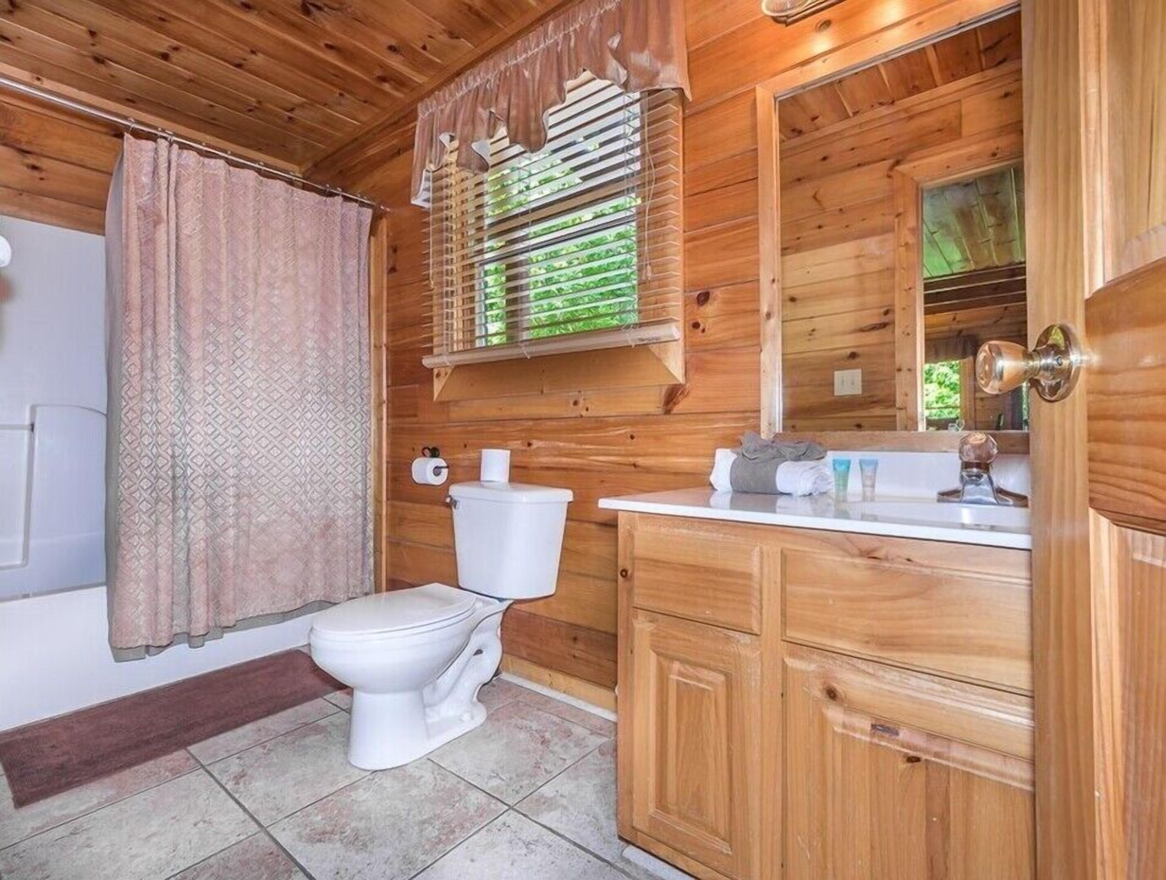 A wooden cabin bathroom with a toilet, sink, and window with blinds.