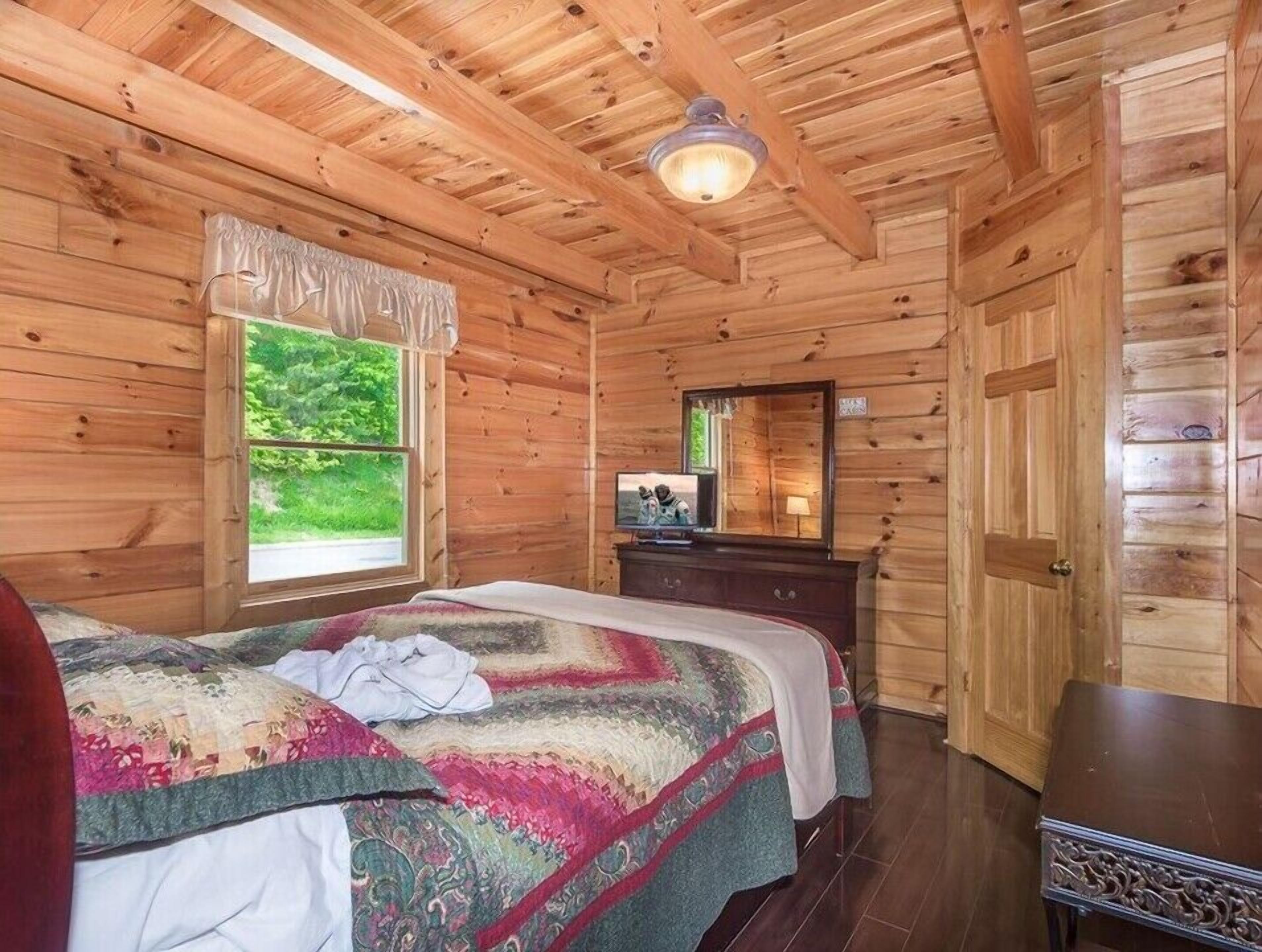 Un dormitorio de cabaña de madera con una cama, cómoda y ventana con vistas a la vegetación.