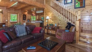 A wooden cabin interior with a living room, kitchen, and a staircase.