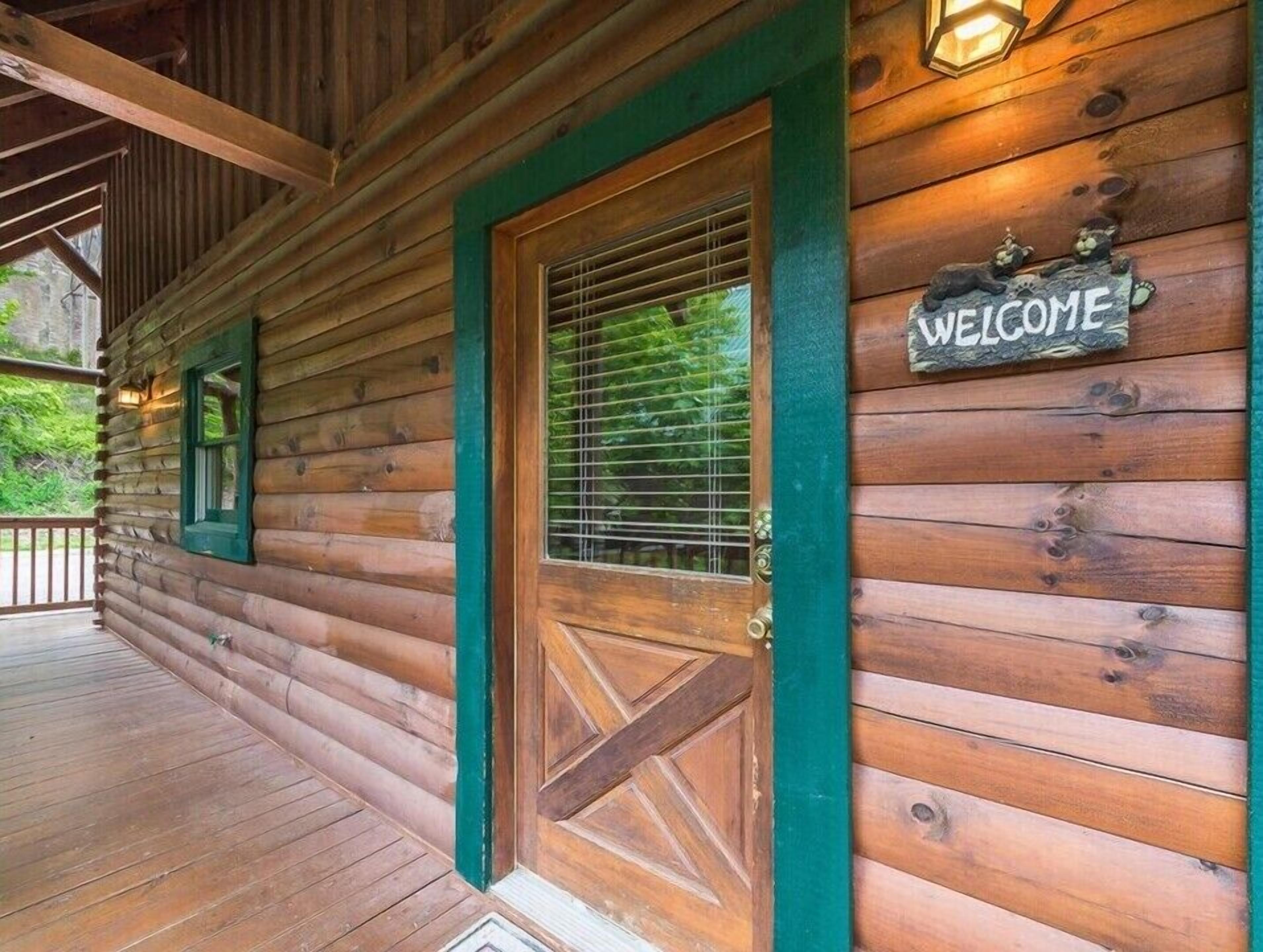 A wooden cabin with a porch, a welcome sign, and a window with blinds.