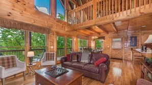 A spacious wooden cabin with a high ceiling, a balcony, and a cozy living area with a couch, chairs, and a coffee table.
