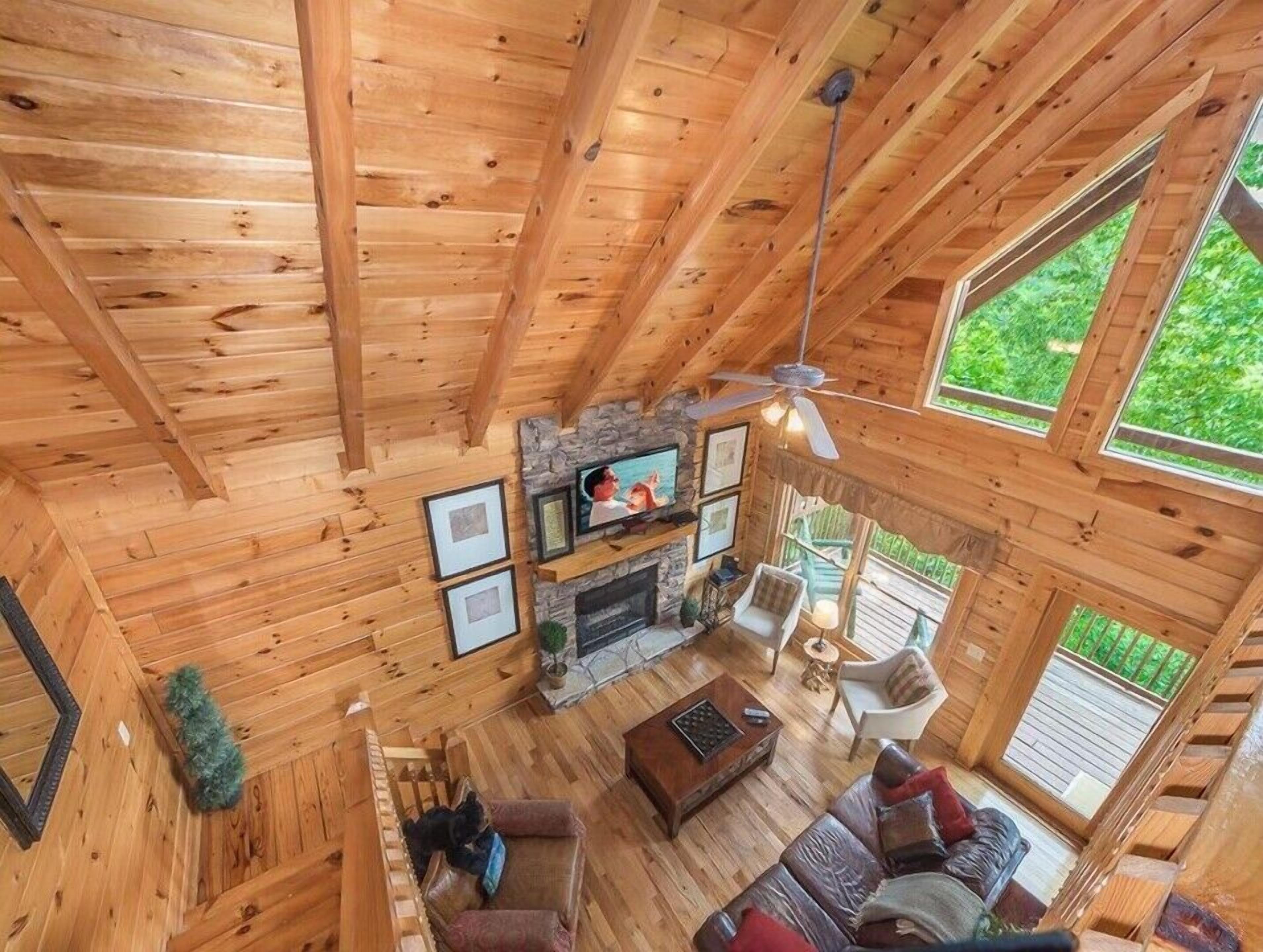 Ein geräumiges Holzhäuschen im Inneren mit Kamin, Deckenventilator und großen Fenstern, die einen Blick ins Freie ermöglichen.