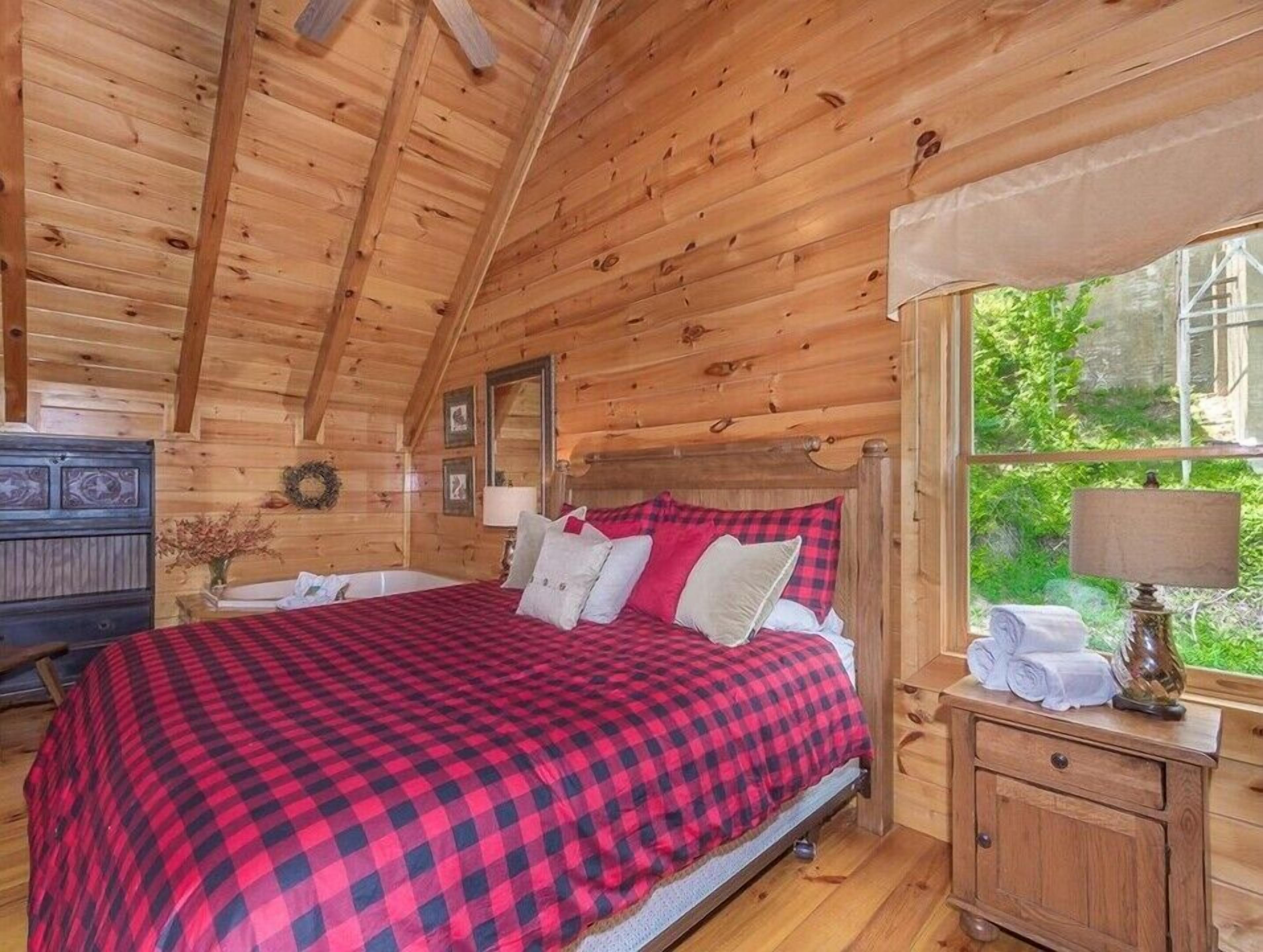 Een knus houten slaapkamer met een bed, een kast en een raam met uitzicht op groen.