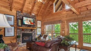 A cozy cabin interior with a stone fireplace, leather sofa, and a television mounted above it.