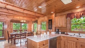 A wooden cabin with a kitchen, dining area, and large windows.