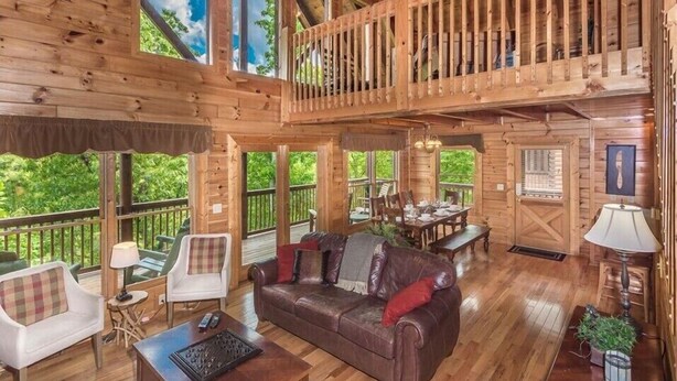 A spacious cabin with a dining area, a living room with a sofa and chairs, and a balcony with a railing.