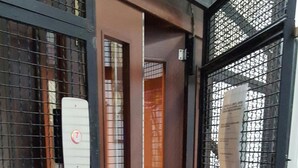 Un hueco de ascensor estrecho con una puerta de metal y una puerta de malla a la derecha.