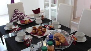 Una mesa de desayuno con tazas, platos, muffins, croissants y una cafetera.