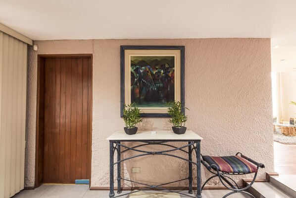 A room with a wooden door, a framed abstract painting, a small table with two potted plants, and a cushioned chair. - Lima Fabulous  House 5br sleep8 Next Mall (Lima)
