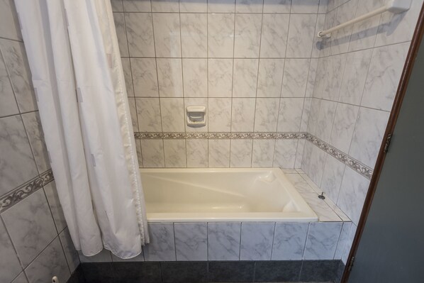 Un baño con bañera, cortina de ducha y paredes de azulejos.