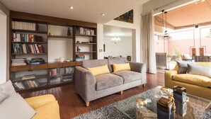A modern living room with a grey sofa, yellow cushions, a glass coffee table, and a bookshelf filled with books. - Lima Fabulous  House 5br sleep8 Next Mall (Lima)
