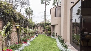 A well-maintained garden with a variety of plants and flowers, a brick wall, and a modern building with large windows. - Lima Fabulous  House 5br sleep8 Next Mall (Lima)