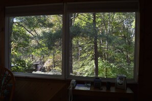 Enjoy a peaceful forest view from the room's large window, featuring a desk with a telephone, clock, and papers.