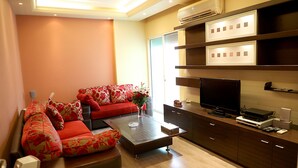 A modern living room with a red sofa, a coffee table, a flat-screen TV, and built-in shelves. - Vino Apartment (Zalqa)